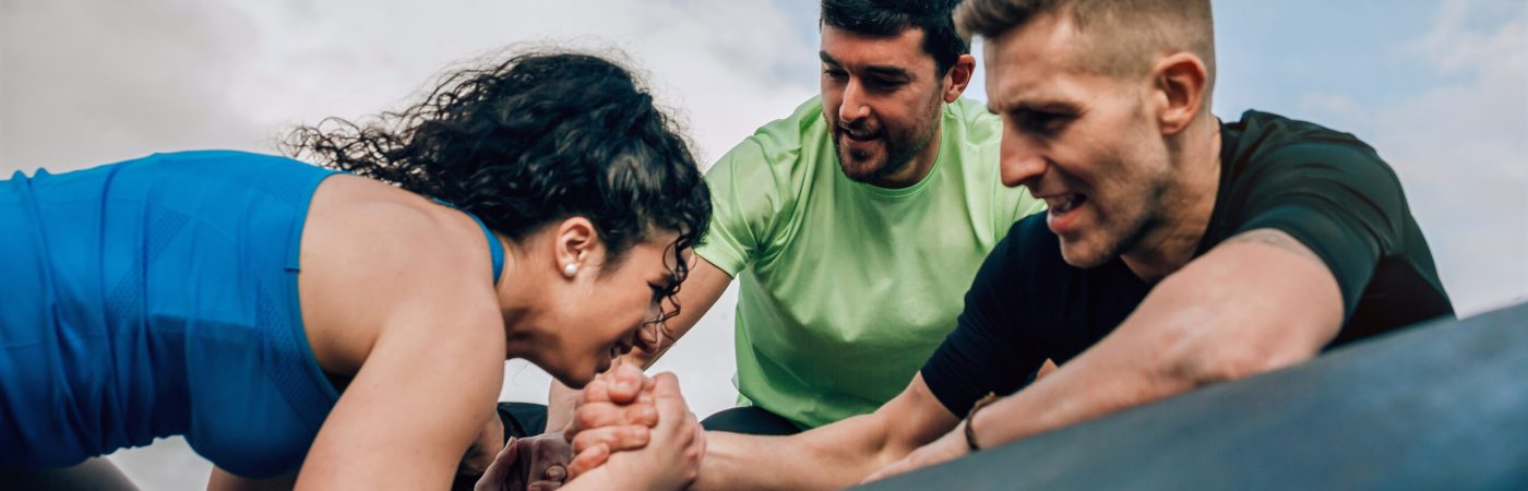 Female participant in an obstacle course climbing a drum helped by her teammates